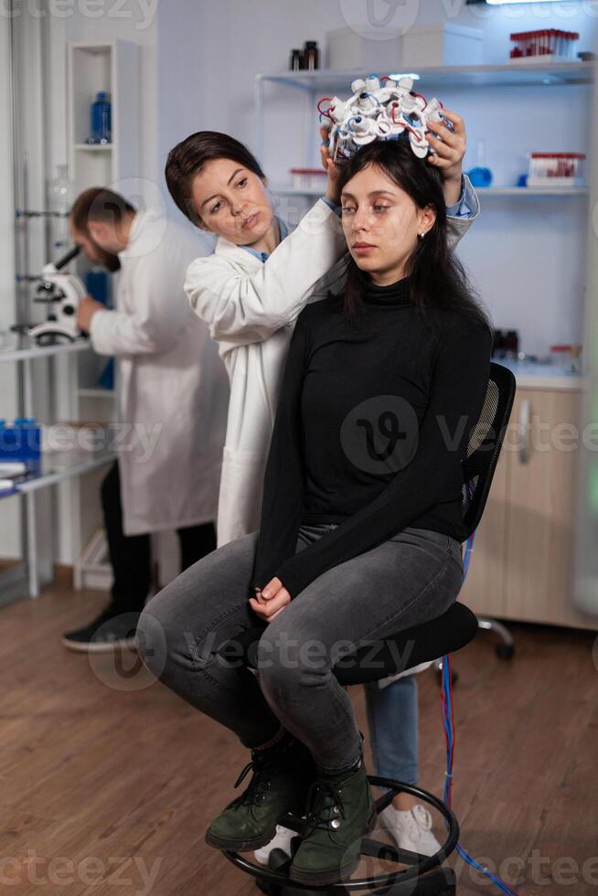 Woman patient standing on chair in neurology laboratory during clinical experiment while specialist researcher putting medical eeg scanner on head monitoring brain activity. Nervous system evolution photo