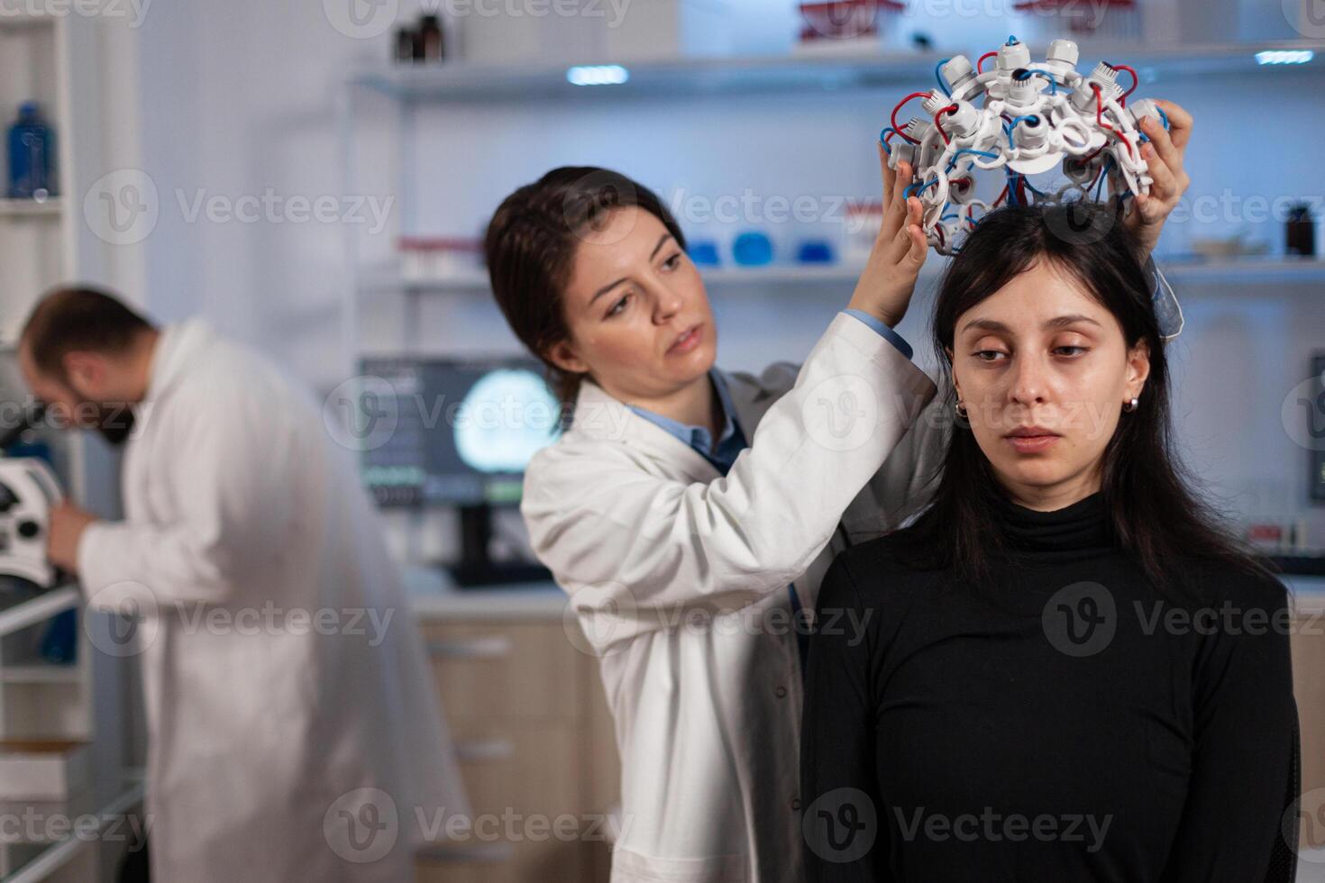 Neurologist doctor woman putting eeg scanner on patient head analyzing brain evolution working at disease diagnosis during neurology experiment in high tech lab. Scientist doctor explaining tomography photo