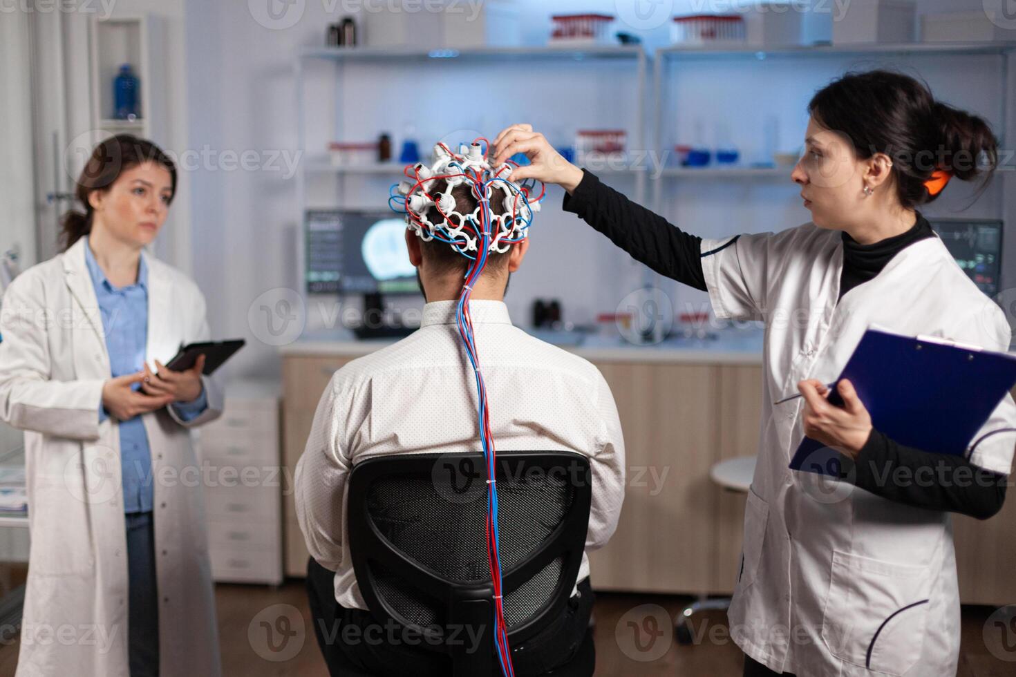 Medical team of neurologists adjusting brain eeg analyzing nervous system evolution of man patient during clinical experiment in neuroscience laboratory. Physician doctor monitoring neurology activity photo