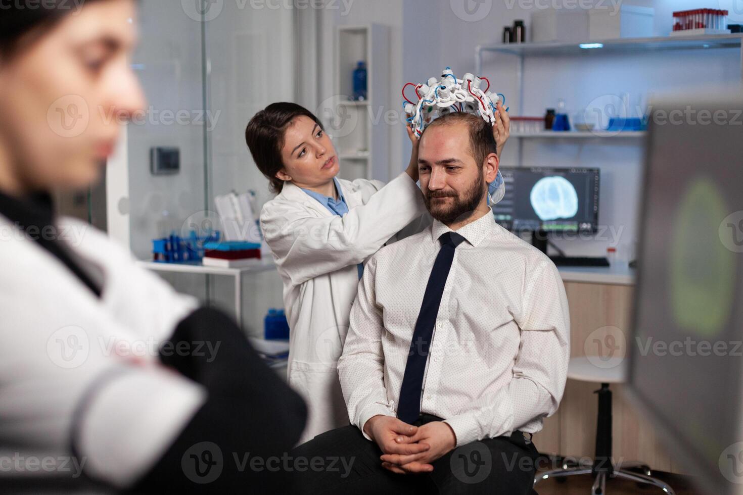 Specialist neurologist woman adjusting eeg headset analyzing brain activity of man patient monitoring nervous system information in medical laboratory. Physician doctor doing neurology experiment photo