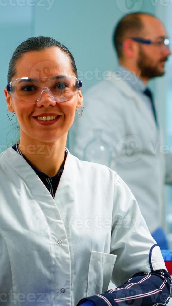Laboratory doctor looking at camera smiling in modern equipped lab. Multiethnic team examining virus evolution using high tech and chemistry tools for scientific research, vaccine development. photo