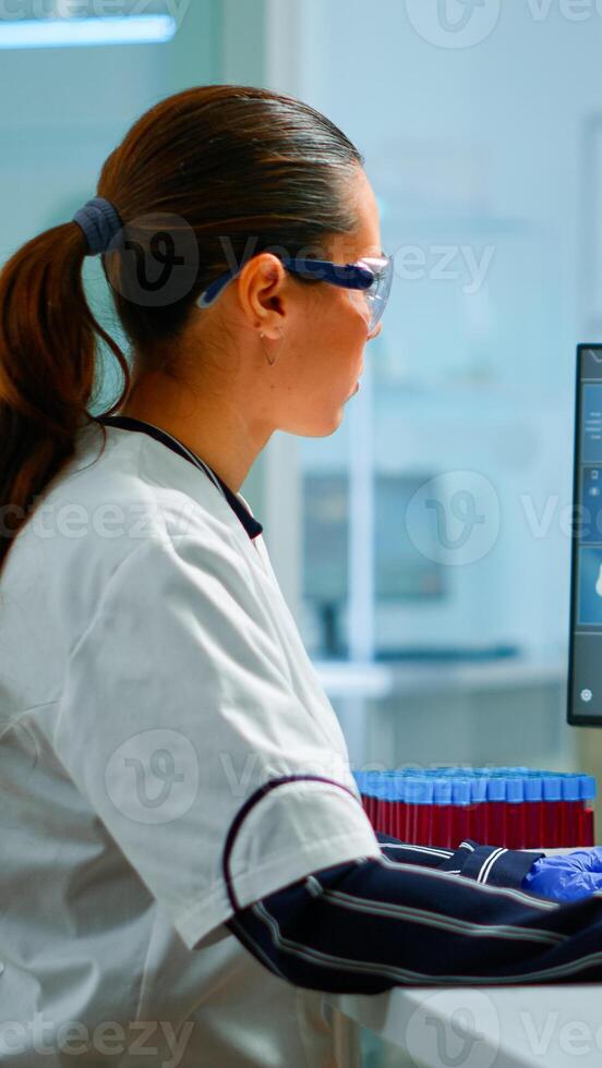 Biologist doctor checking DNA informations typing on pc in modern equipped laboratory. Scientists examining vaccine evolution in medical lab using high tech, chemistry tools for scientific research. photo