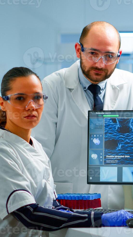 Team of scientists sitting in laboratory looking at camera in modern equipped lab. Group of doctors examining virus evolution using high tech for scientific research, vaccine development. photo
