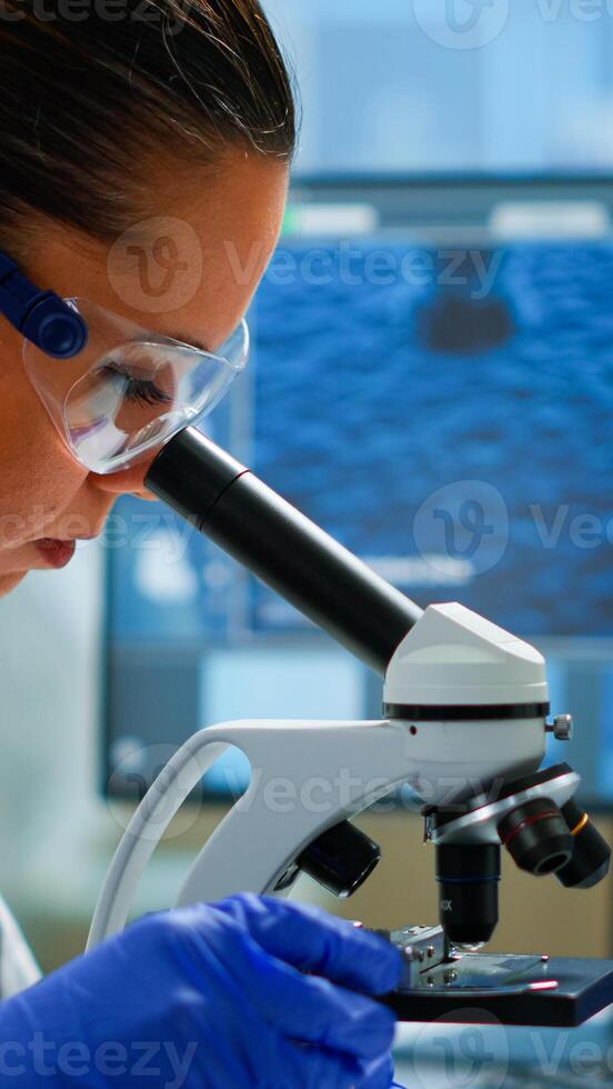 Portrait of scientist looking under microscope in medical development laboratory, analyzing petri dish sample. Medicine, biotechnology research in advanced pharma lab, examining virus evolution photo