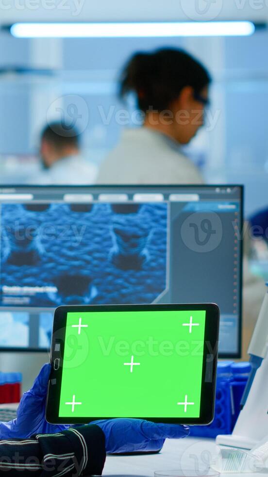 Medical research scientist working on tablet with green screen mock up template in applied science lab. Engineers conducting experiments in background, examining vaccine evolution using high tech photo