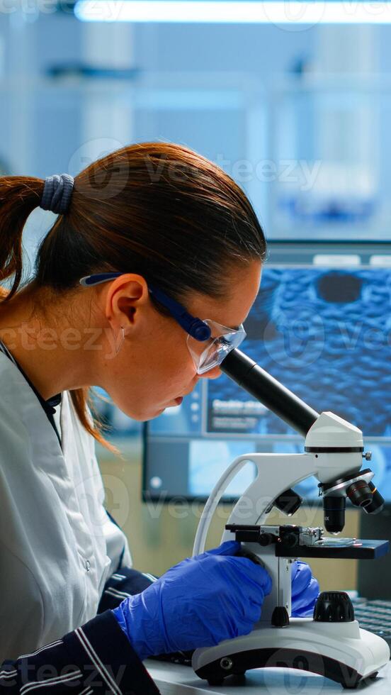 Scientist looking at biological samples under microscope typing on pc. Team of chemists working in lab, examining virus evolution using high tech for scientific research of vaccine development. photo