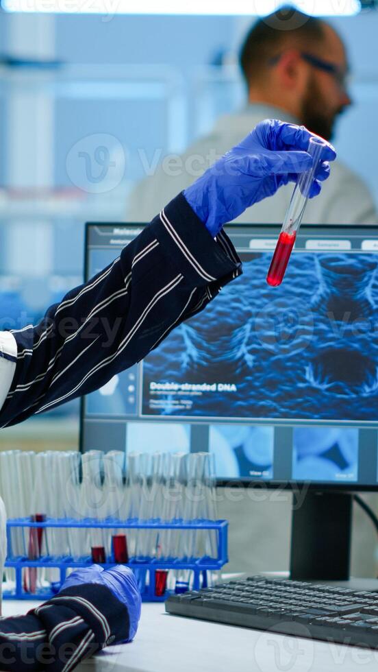 Scientist doctor looking at blood sample and typing on computer while coworker opening door using digital computer with touch scan. Woman examining virus evolution using high tech and chemistry tools photo