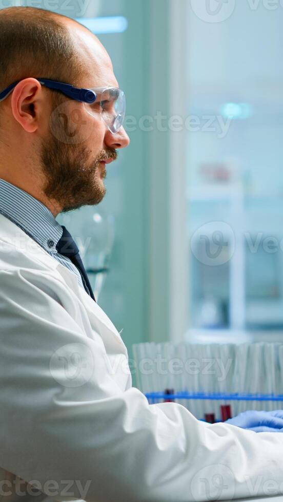 Scientist in lab coat analysing blood sample from test tube. Viorolog researcher in professional laboratory working to discover medical treatment, team of doctors analysing vaccine evolution photo