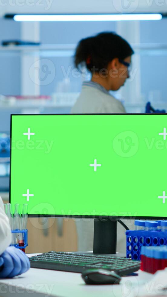 Researcher looking at chroma key display in modern equipped lab analysing virus evolution. Team of microbiologists doing vaccine research writing on device with green screen, isolated, mockup display. photo