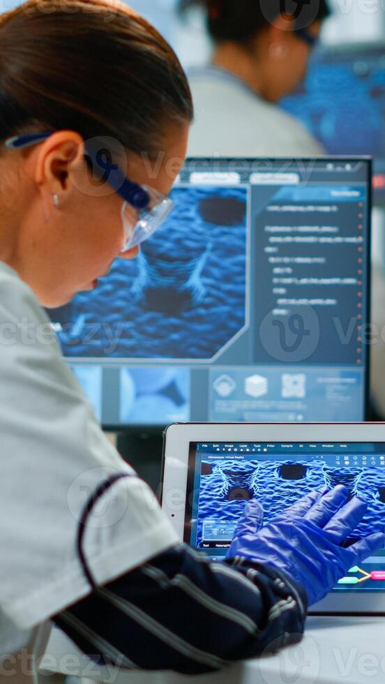Scientist using digital tablet working in modern medical research laboratory, analyzing DNA information. Medicine, biotechnology research in advanced pharma lab, examining virus evolution photo