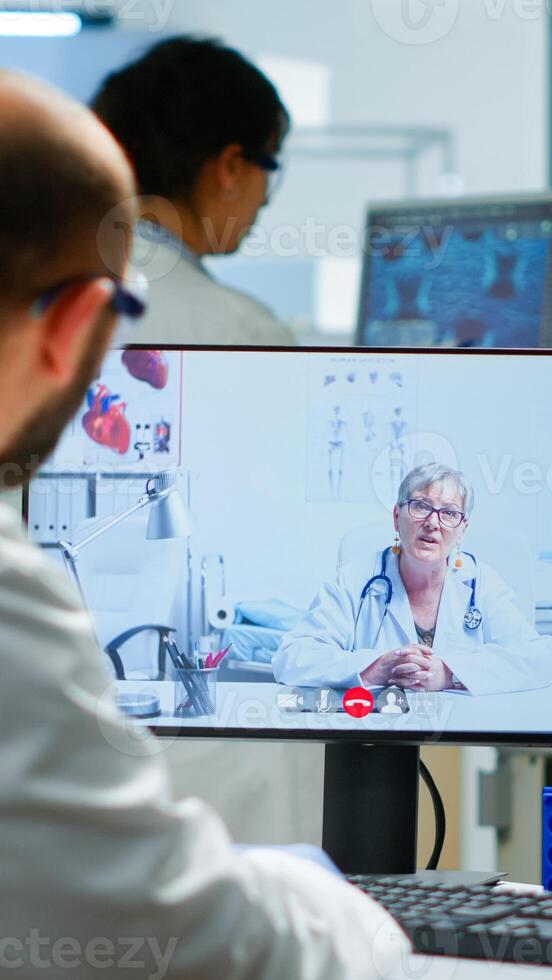 Senior woman doctor offering medical online advices to chemist using pc webcam. Scientist holding blood sample during online discussion, virtual conference, helping on telemedicine, healthcare support photo