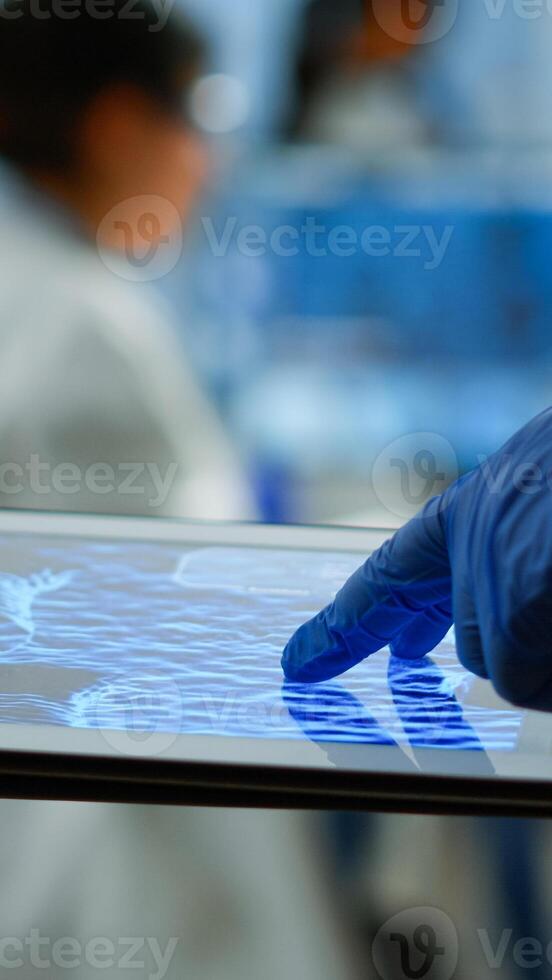 Close up of researcher using tablet, pointing, analysing DNA informations standing in medical laboratory. Viorolog doctor working to discover medical treatment, vaccine development, virus evolution photo