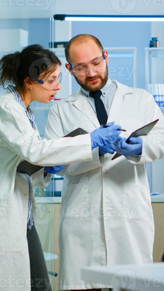 Scientists coworkers using digital tablet working in medical research laboratory, analysing biochemicals samples, talking. Scientific lab for medicine, microbiology development with advanced equipment photo