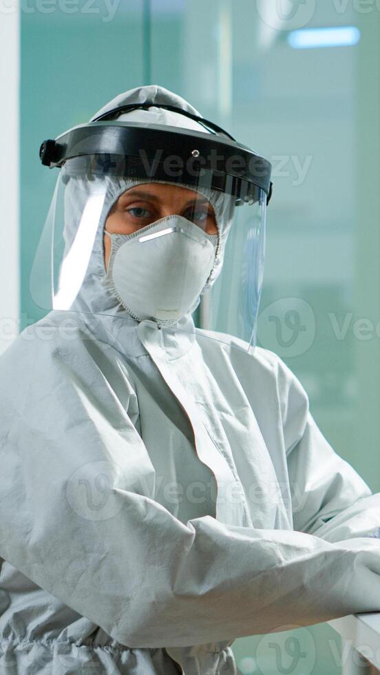 Portrait of tired scientist in coverall looking at camera sitting in modern equipped laboratory. Team of doctors examining virus evolution using high tech and chemistry tools for vaccine development. photo