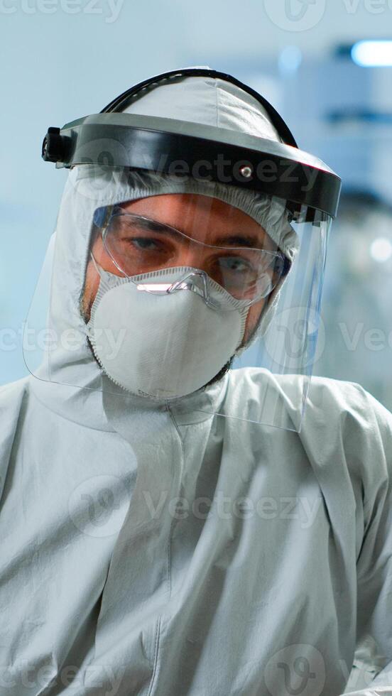 Close up of tired chemist doctor in coverall looking at camera working in scientific laboratory. Scientist working with various bacteria, tissue and blood samples, pharmaceutical research for antibiotics photo