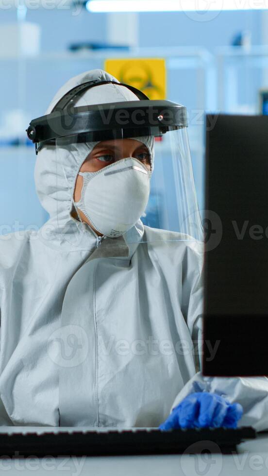 Laboratory technician assistant in ppe suit analyzing blood sample in test tube typing at pc. Doctor working with various bacteria, tissue, pharmaceutical research for antibiotics against covid19. photo