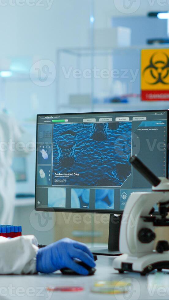 Chemist in ppe suit typing on pc checking vaccine development in modern equipped laboratory. Doctor working with various bacteria, tissue and blood samples, pharmaceutical research for antibiotics photo