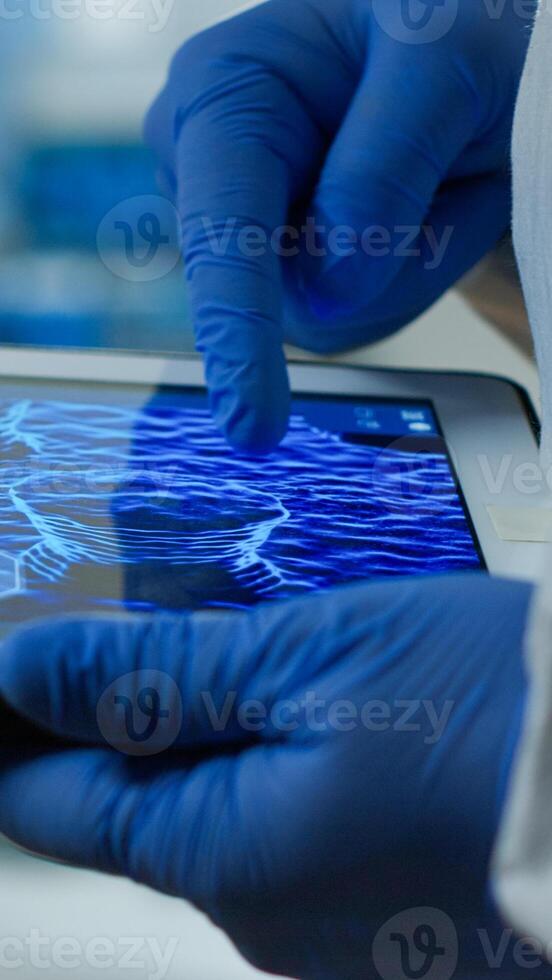 Close up of chemist doctor working on tablet with DNA scan image analysing treatment results. Scientist examining virus evolution using high tech researching vaccine development against covid19 photo