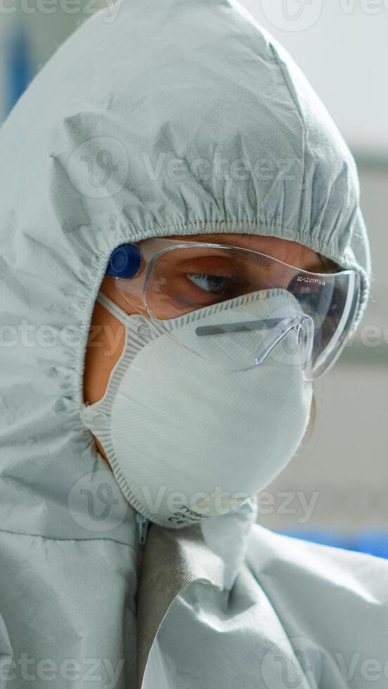 Scientist in coverall doing research analysing liquid in tube at modern equipped laboratory. Biochemist examining vaccine evolution using high tech for treatment development against covid19 virus photo