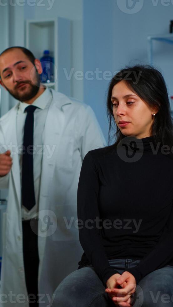 Woman waiting doctor sitting on chair in neurological research laboratory, while researchers team discussing in background health status of patient, brain functions, nervous system, tomography scan photo