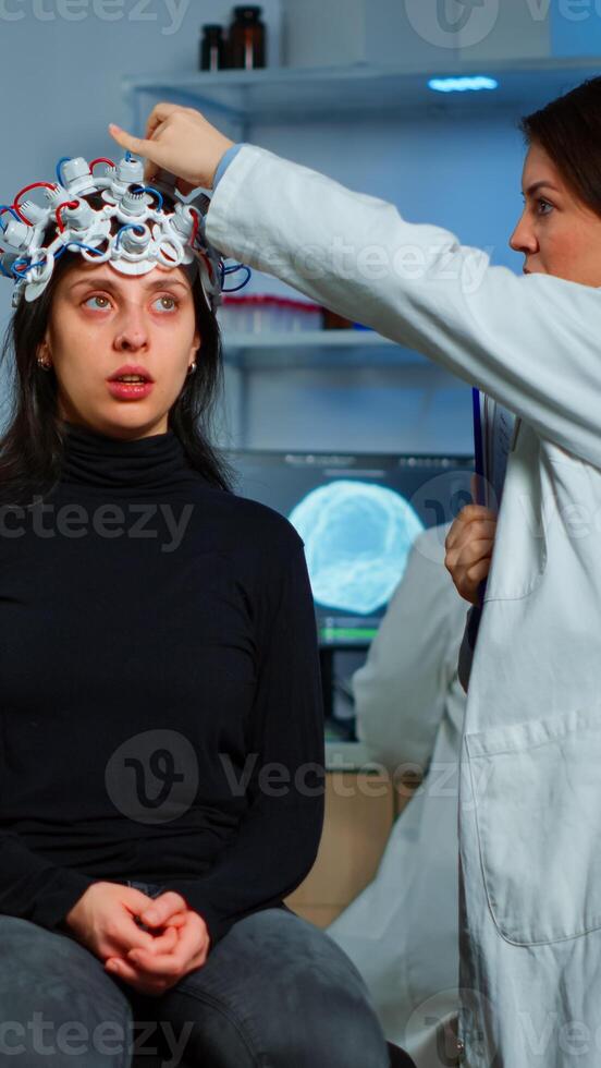 Doctor researcher adjusting EEG headset analyzing patient's evolution after treatment against disease of nervous system. Team of scientists working late night in neurological research laboratory photo
