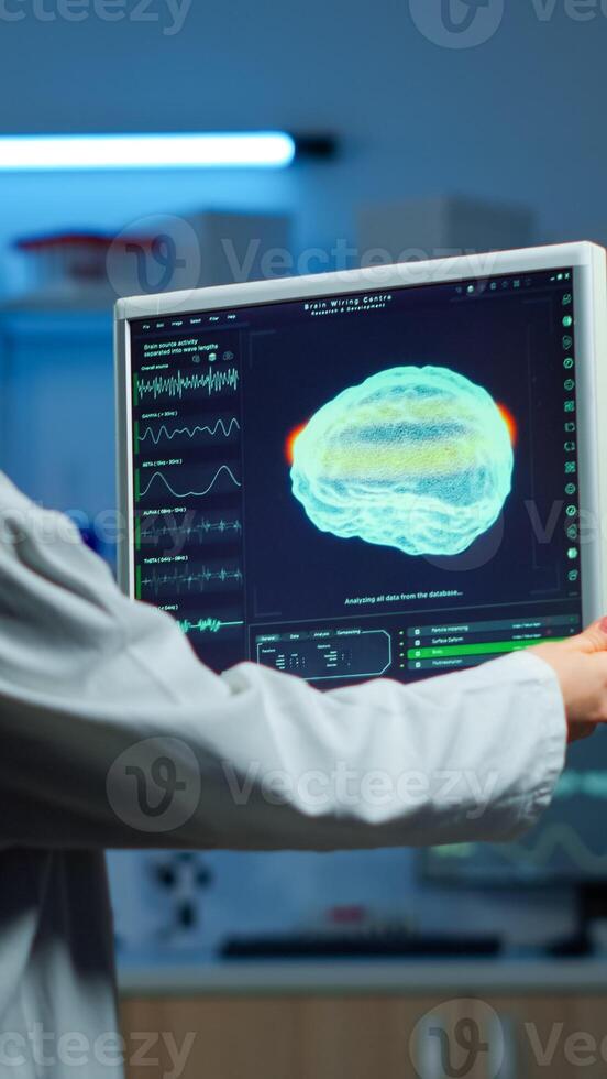 Neurologist doctor reading informations of patient looking at monitor analysing brain scan discussing with patient wearing eeg headset. Scientist taking notes examining nervous system of woman in lab photo
