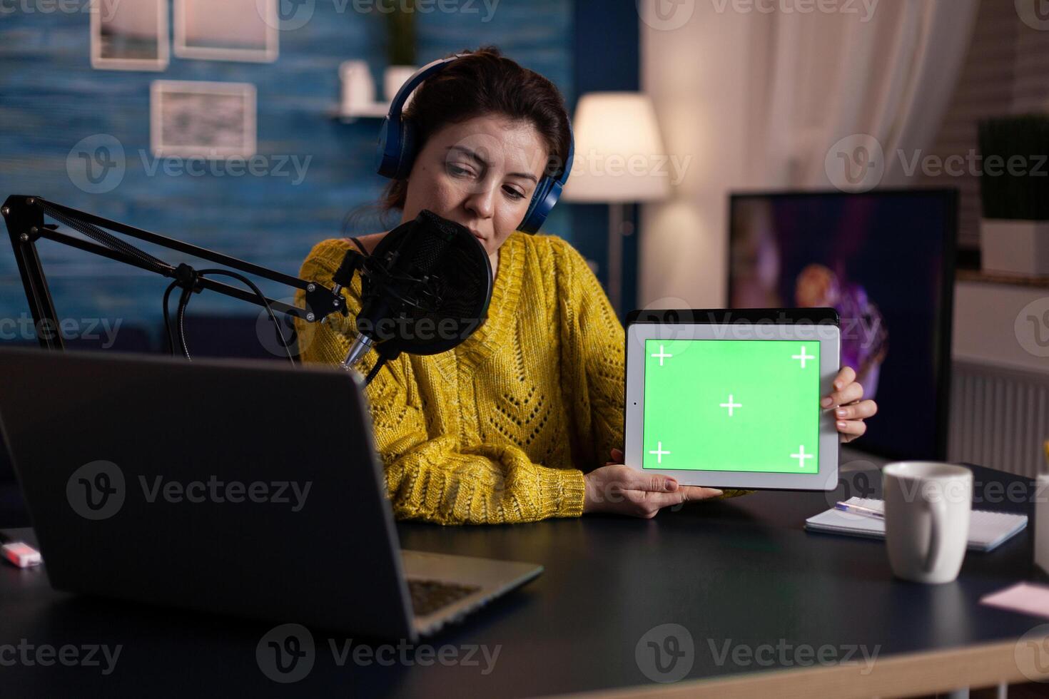 Social media influencer talking with fans into microphone showing mock up green screen chroma key tablet with isolated display at camera during online livestream. Vlogger recording on-air show photo