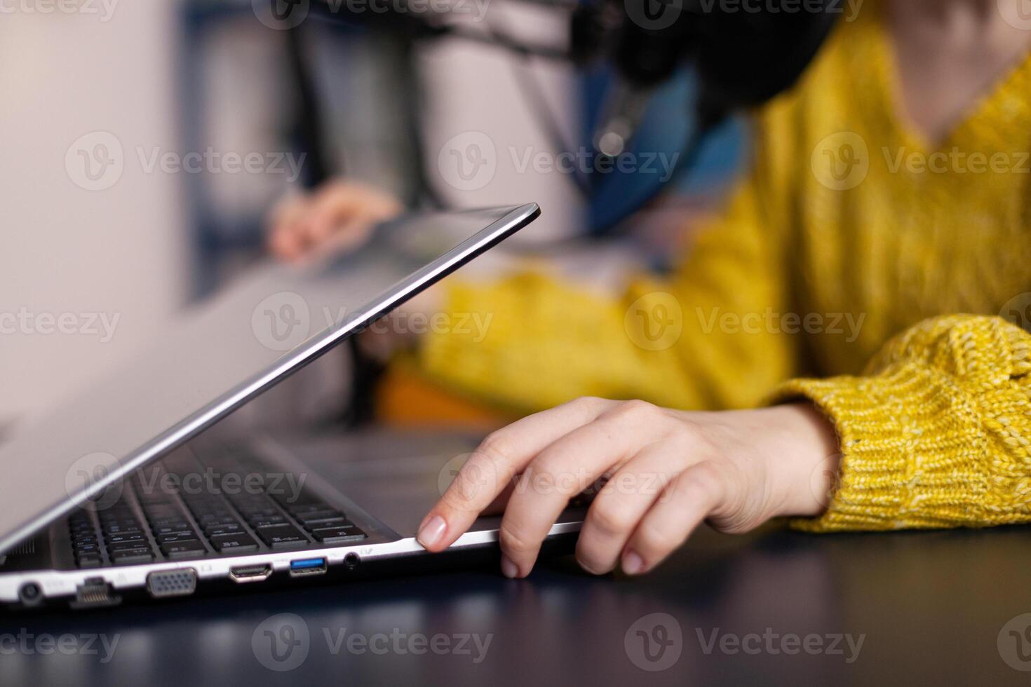 Vlogger woman opening laptop talking into professional microphone recording online podcast sitting at desk in podcasting studio at home. Social media influencer podcasting on-air studio photo