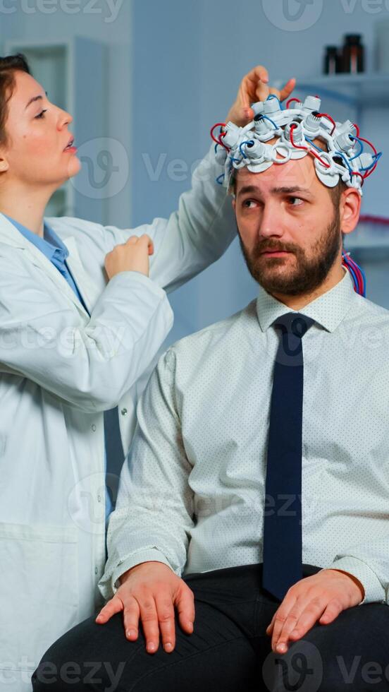 Patient with brain scan discussing with researcher neurological doctor while adjusting brainwave scanning headset examining diagnosis of disease, explaning eeg results, health status, brain functions photo