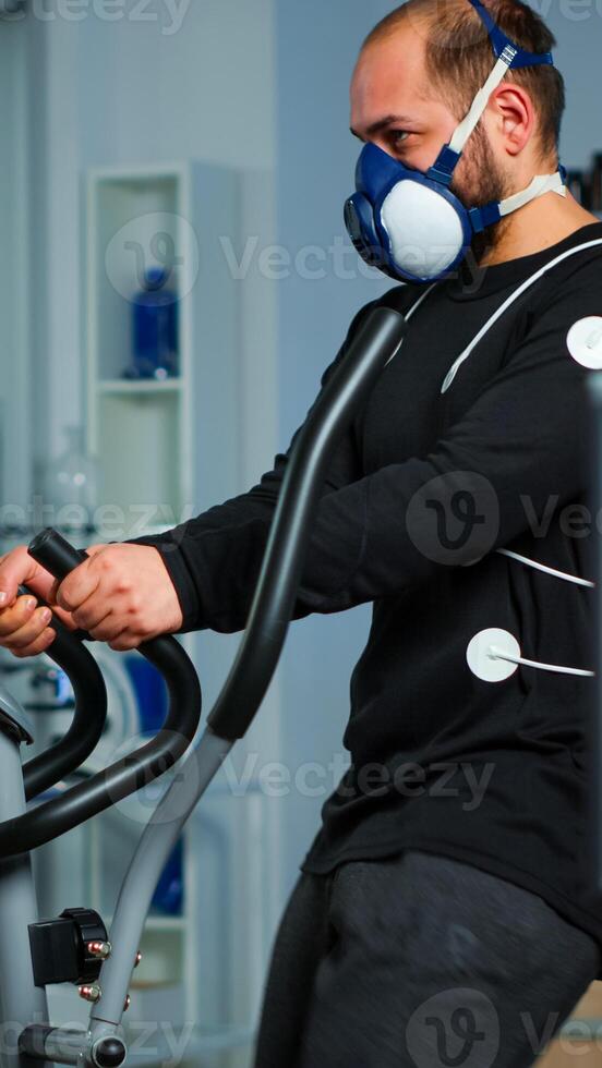 Monitor showing EKG reading of athlete running on cross trainer, while medical specialists supervise exercise, controlling physical activity, measuring heart rate in sports science laboratory photo