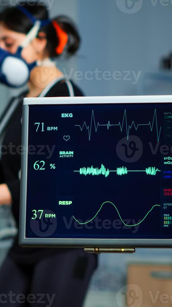 Monitor showing EKG scan of athlete running on cross trainer and medical specialists supervise exercise in background, controlling physical activity, measuring heart rate in sports science laboratory photo