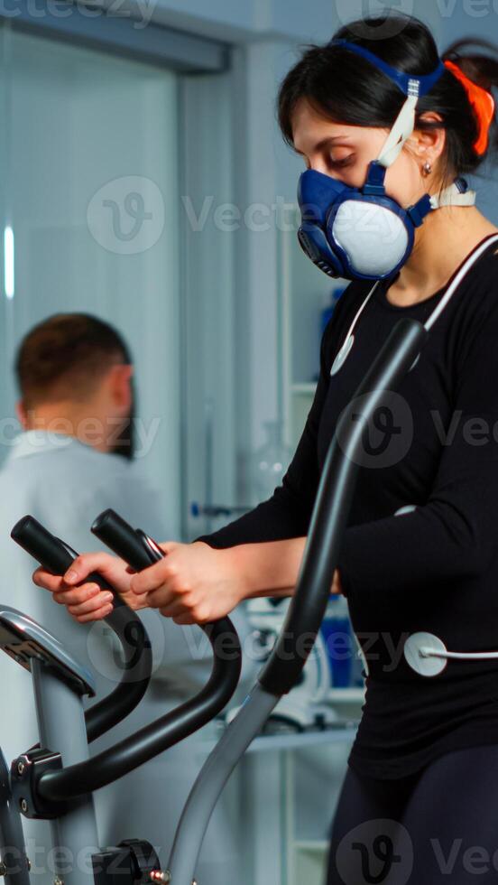 Specialists supervising exercises of patient, reading health information in clipboard, performance athlete running on cross trainer measuring heart rate, phisical endurance, psychological resistance photo