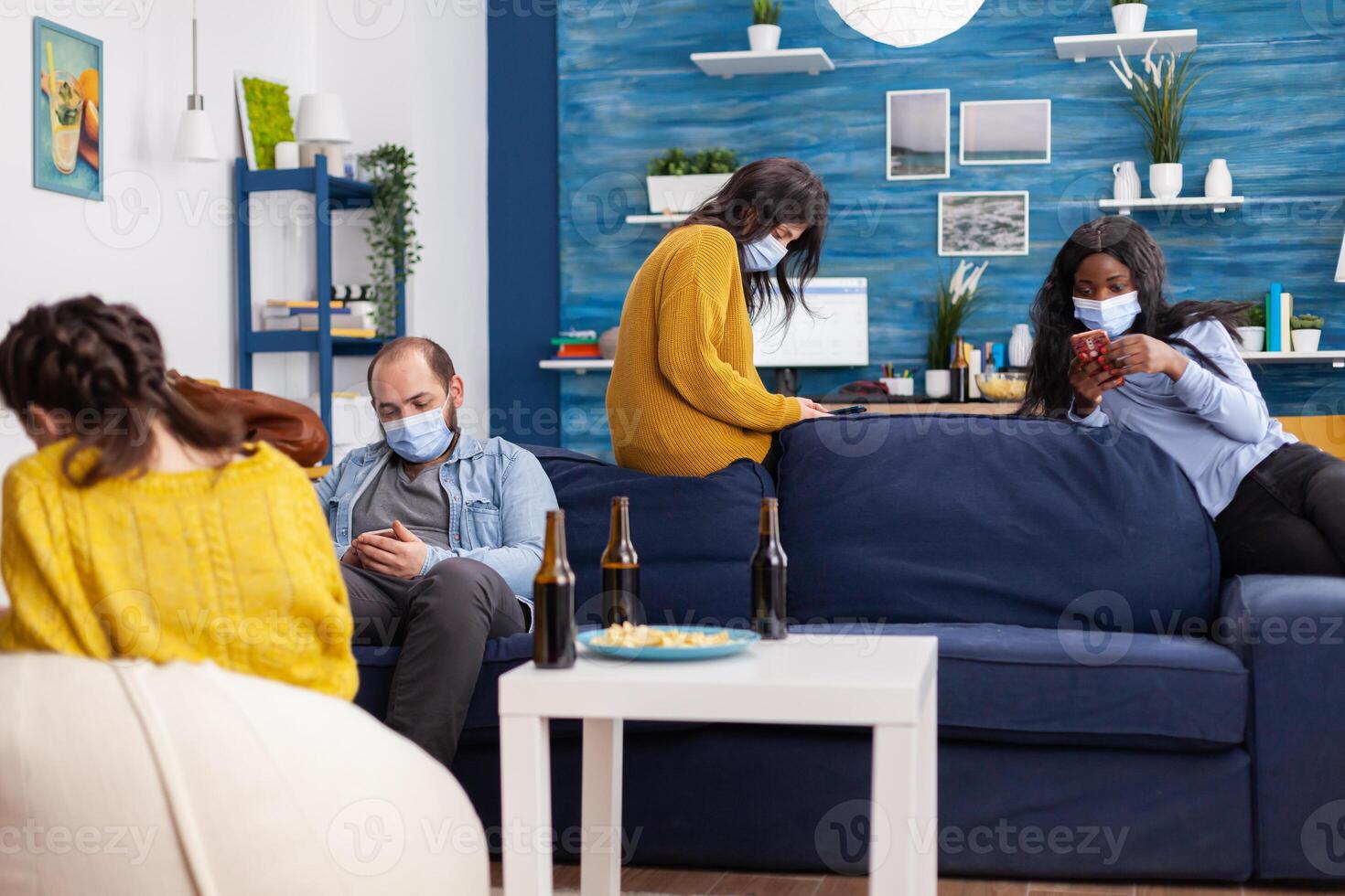 Group of multi ethnic antisocial friends keeping social distancing browsing on smartphones in apartment living room during global pandemic with coronavirus. photo