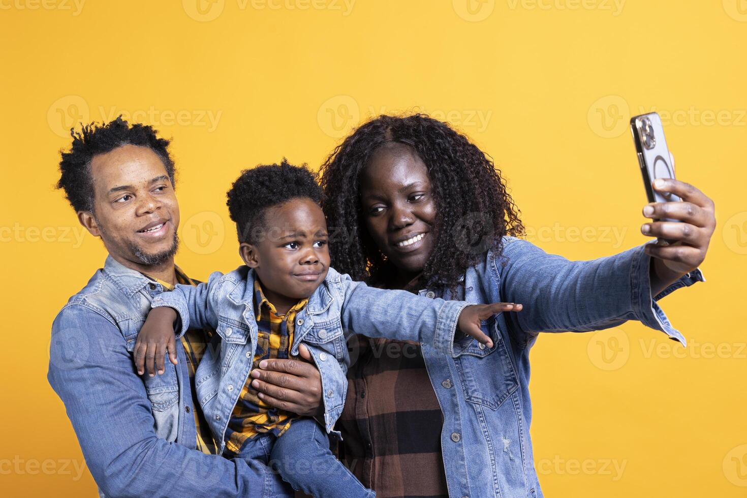 African american parents taking selfies with their small child in studio, posing together and making memories. Young mom and dad enjoying time with their boy, take pictures on phone. photo