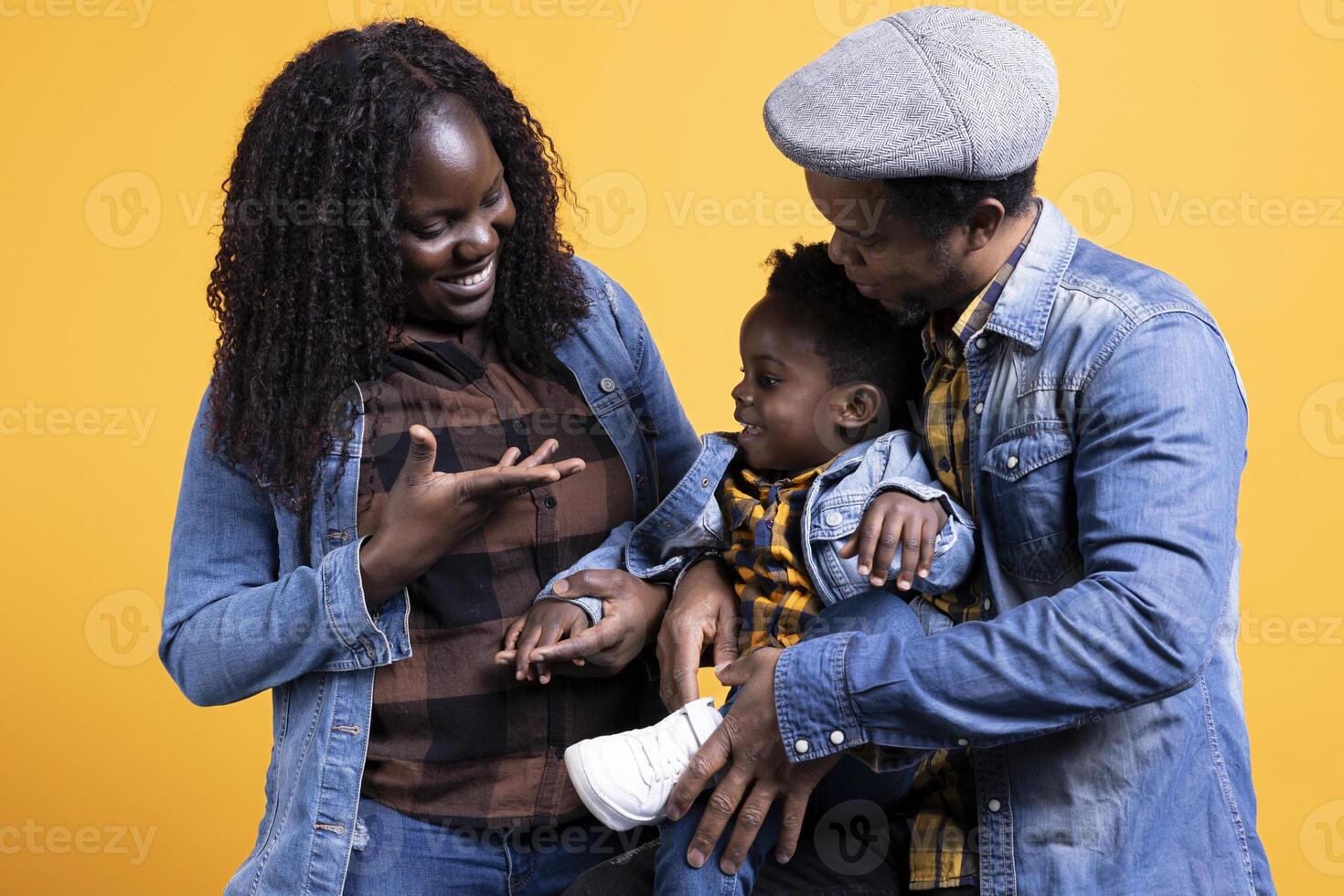 African american young couple embracing their small kid against yellow background. Mother and father feeling happy with their young toddler, showing love and respect for each other. photo