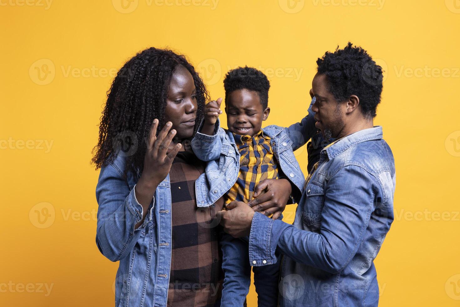 African american family of three smiling against yellow background, posing with affection and gratitude. Cheerful young parents holding their cute infant son, enjoying time together. photo