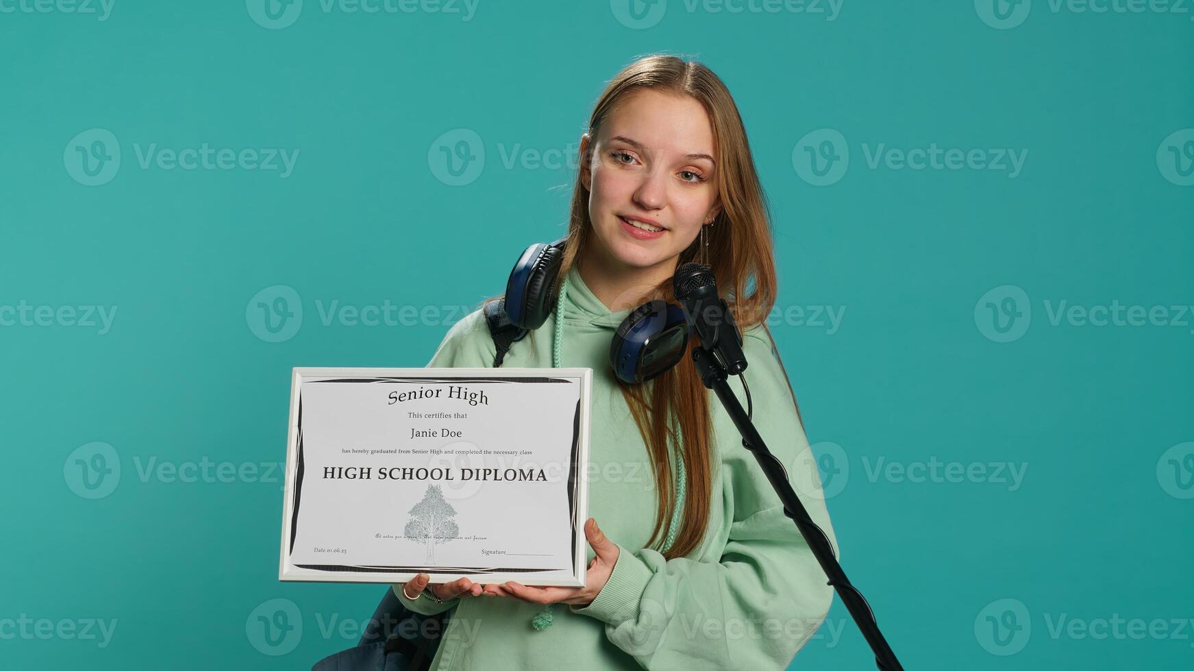 Proud teenage student holding high school diploma, using microphone to thank teachers, studio backdrop. Young girl proud of award, using mic to talk about school degree, camera A photo