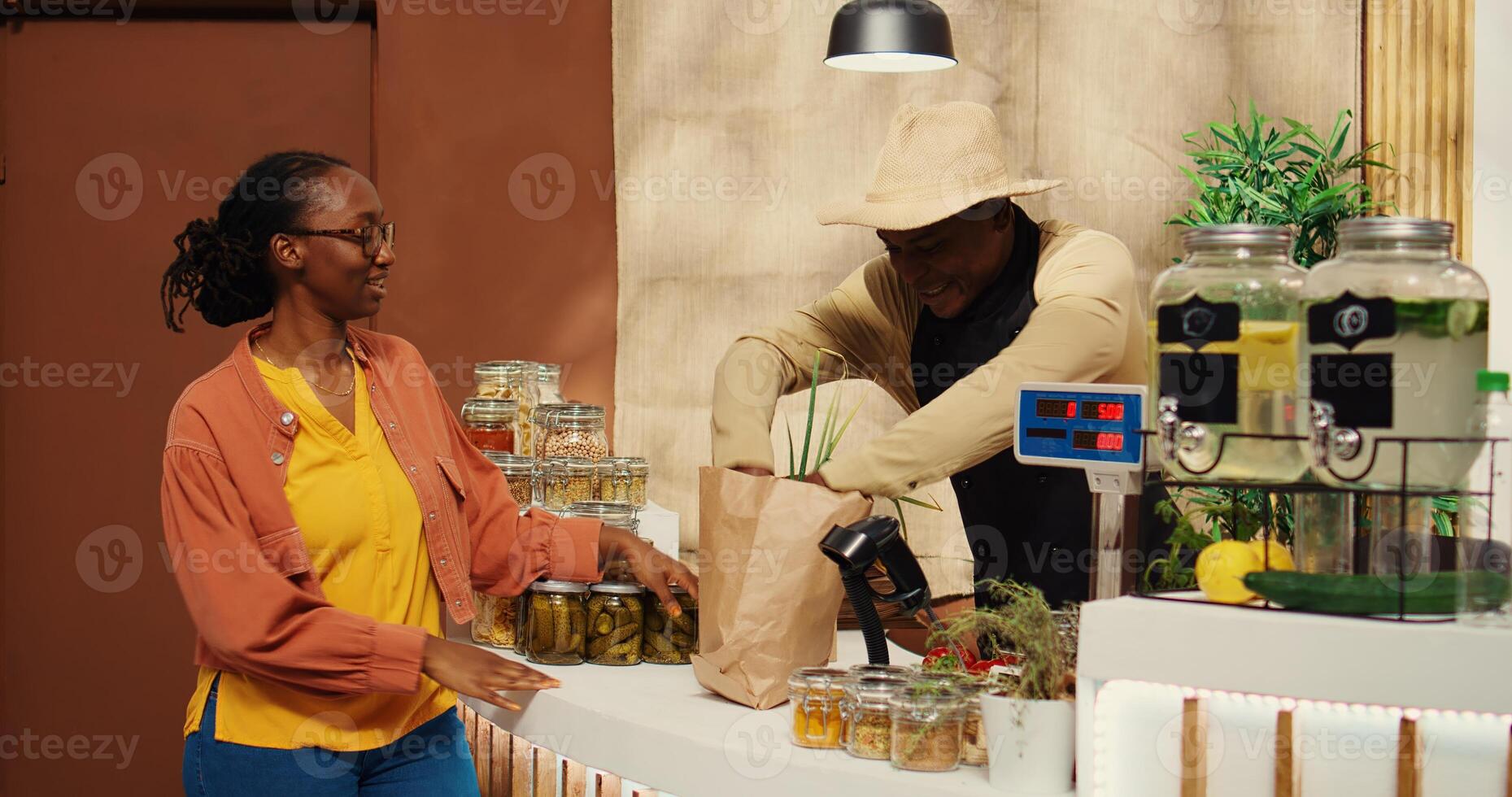 African american vendor weighting produce for regular client at supermarket cash register, using electronic scale to sell locally grown goods. Buyer supporting local farming business. Camera 2. photo