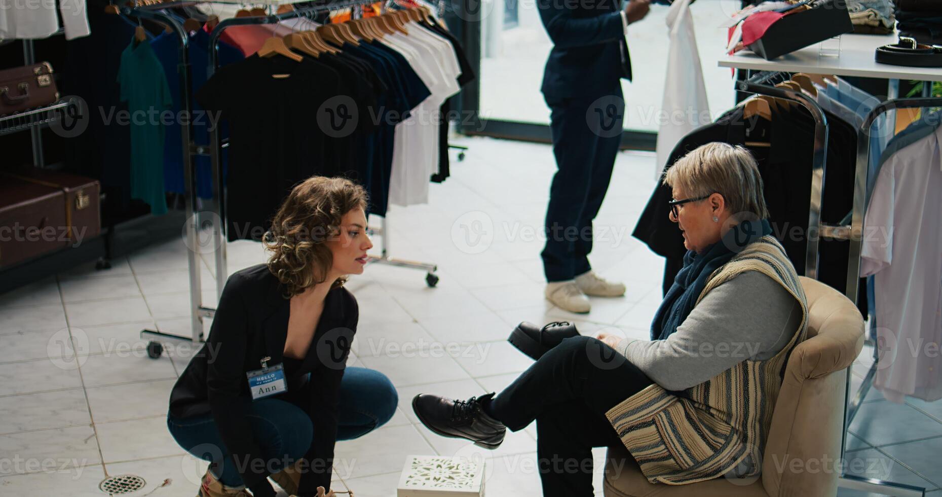 Elderly woman searching for a comfortable pair of shoes at mall, asking retail assistant about available sizes. Store employee recommending various footwear models for senior client. Camera B. photo