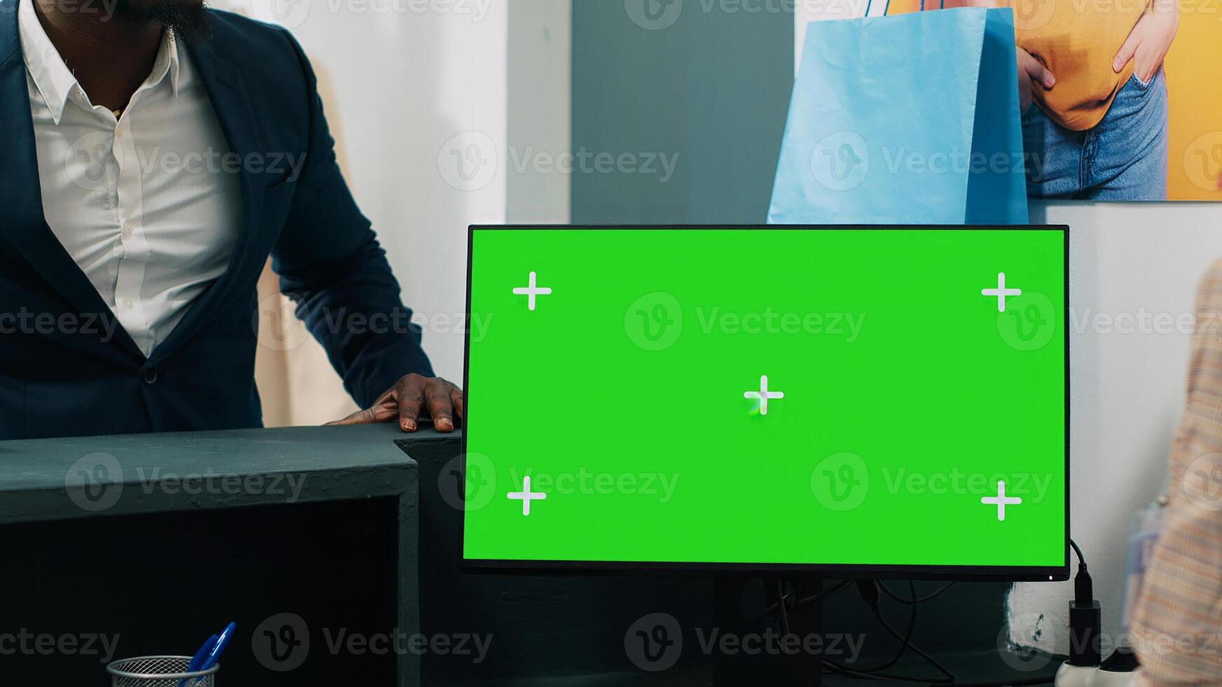 African american worker uses computer with greenscreen display on at checkout counter, putting clothes in a bag for customer. Employee looks at pc showing copyspace mockup screen. Camera A. photo