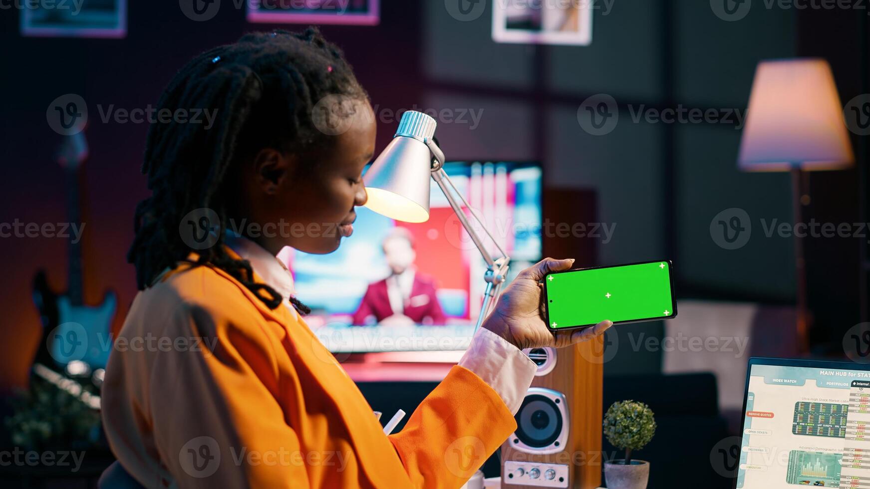 African american girl holds phone with isolated greenscreen at home, studying economics and finances at university. Young woman uses blank mockup template while she works on spreadsheets. Camera A. photo