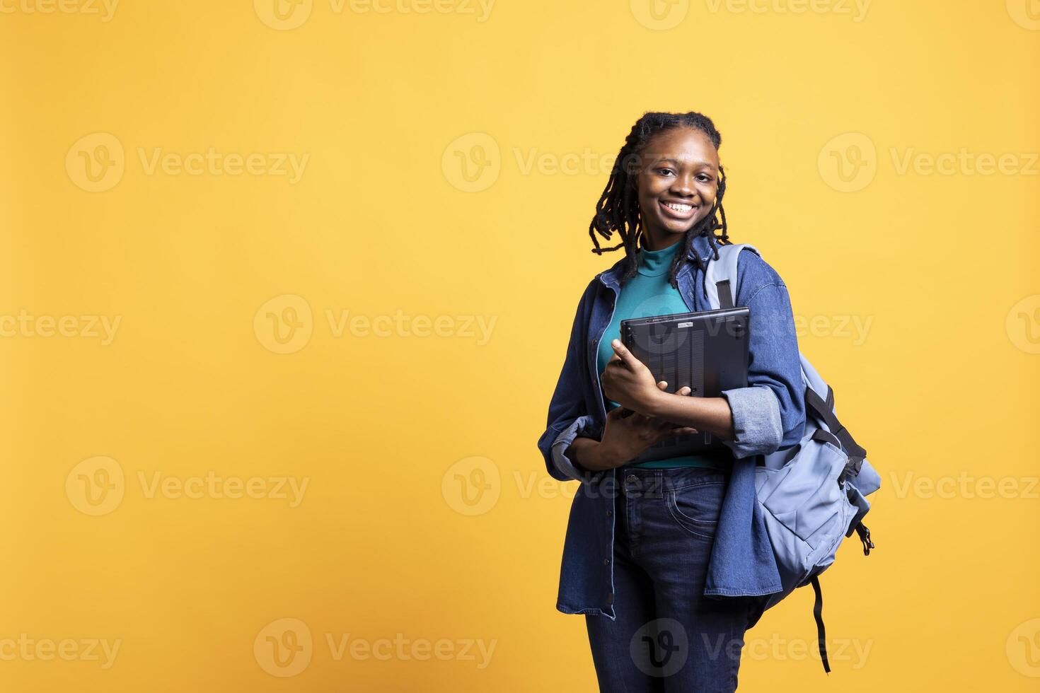 Portrait of cheerful woman carrying laptop needed to do school homework, isolated over studio background. Joyful pupil holding notebook, preparing for university assessment photo