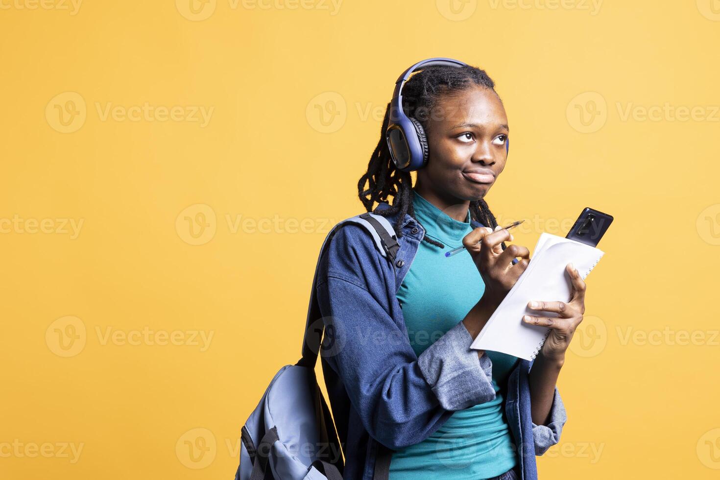 BIPOC student thinking how to solve homework exercises while listening music, isolated over studio background. Girl studying for exam, contemplating and enjoying songs on headphones photo