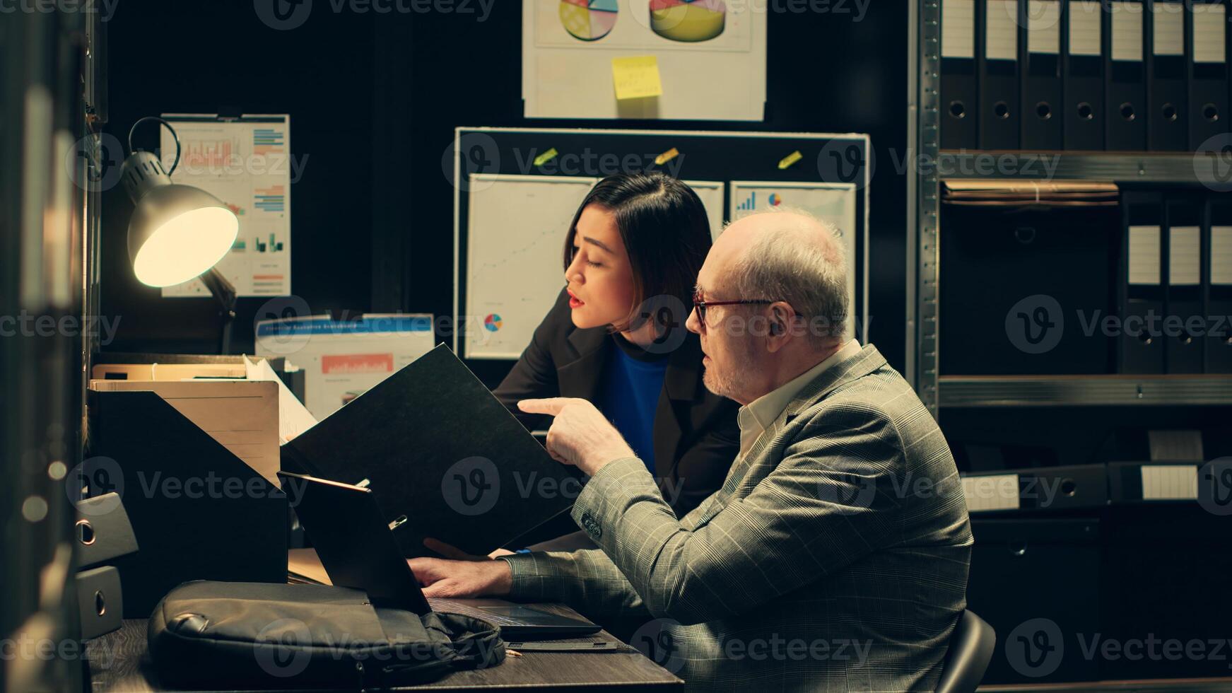 Team members discuss theories while reading past investigations cases to find connections, gathering similar information from old crimes. Law officers collaborating in the archive room. Camera A. photo