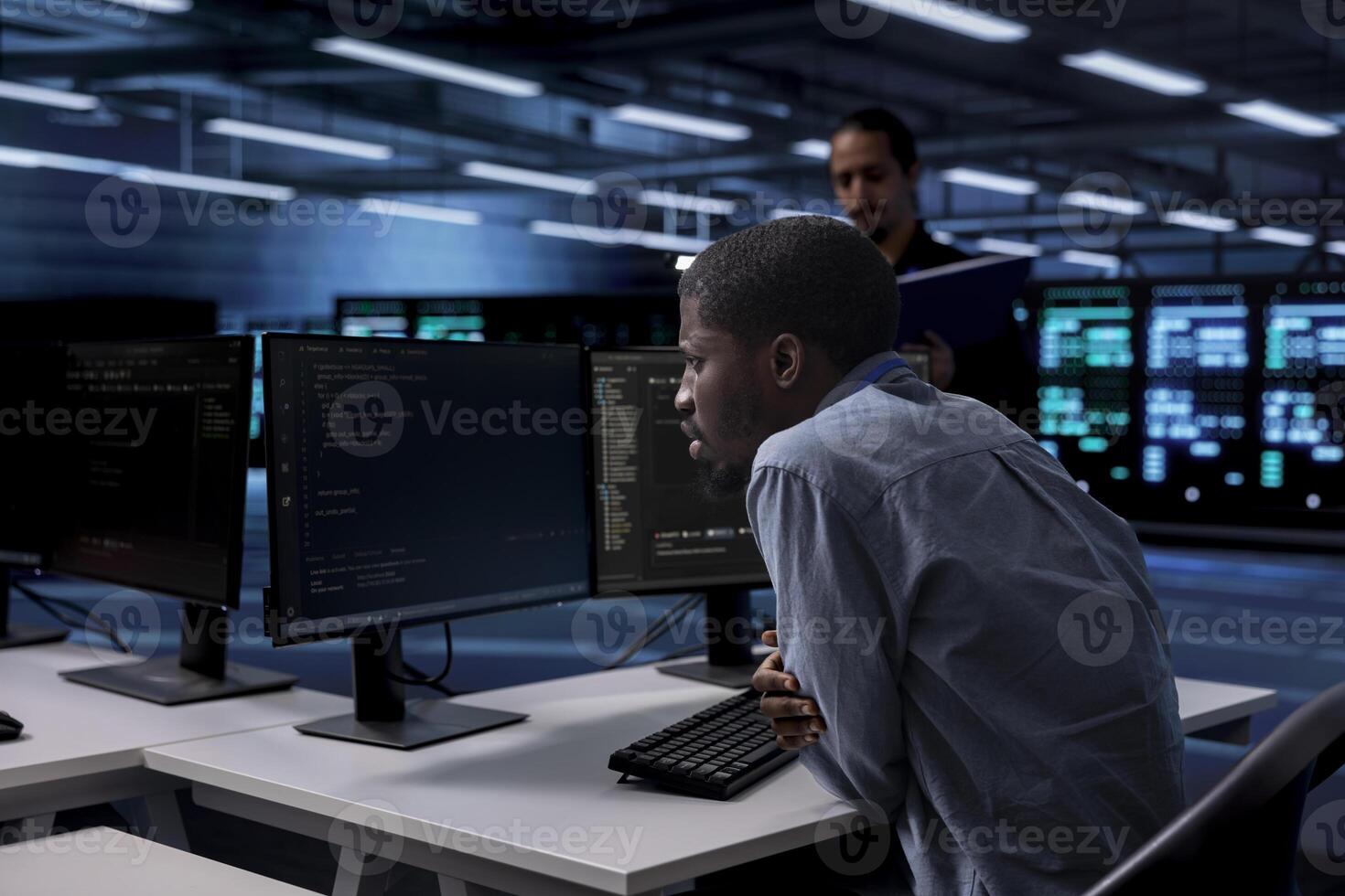 IT engineer in server room facility confused by errors on screen while shielding data from potential threats. Perplexed man puzzled by bugs while safeguarding data center hardware against malware photo