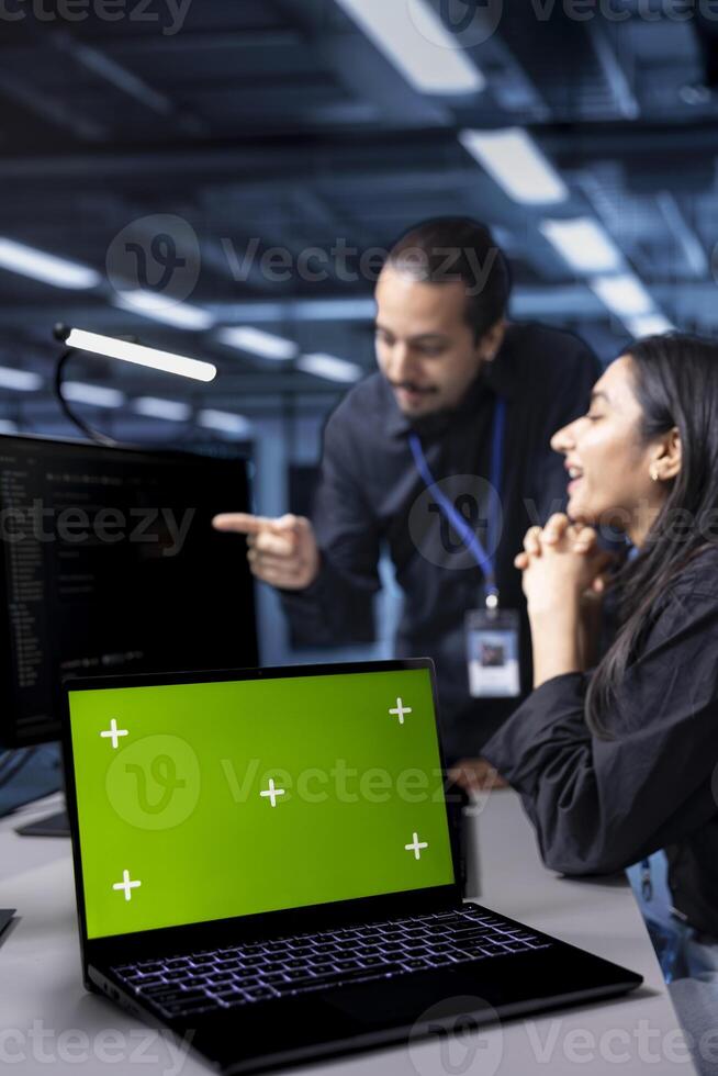 Focus on isolated screen laptop used by system administrators in blurry background to oversee supercomputers. Close up shot of chroma key notebook used by IT expert in server hub establishment photo