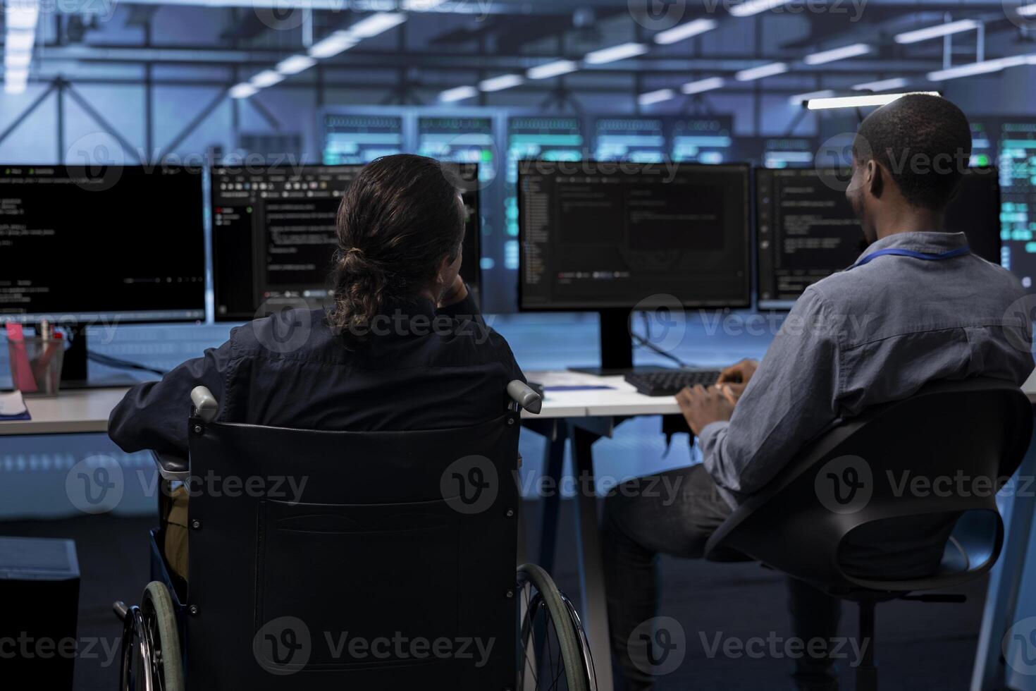 Person with paraplegia and colleague working in inclusive server hub workspace, typing on PC. Woman in wheelchair and coworker doing tasks in data center housing advanced data storage infrastructure photo