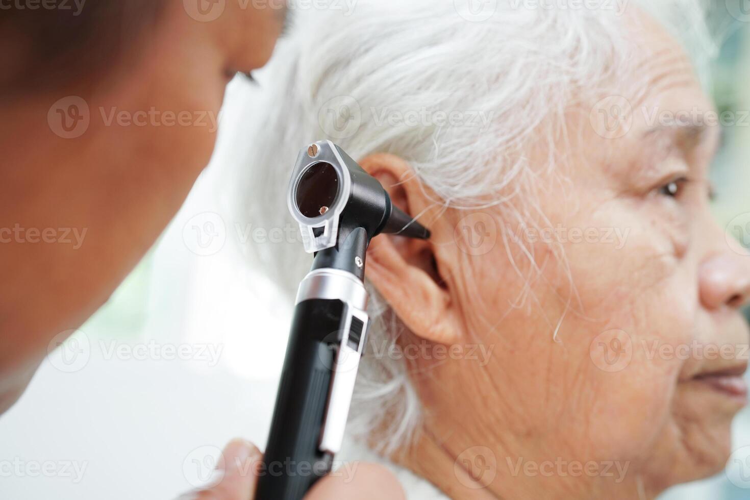 Otolaryngologist or ENT physician doctor examining senior patient ear with otoscope, hearing loss problem. photo
