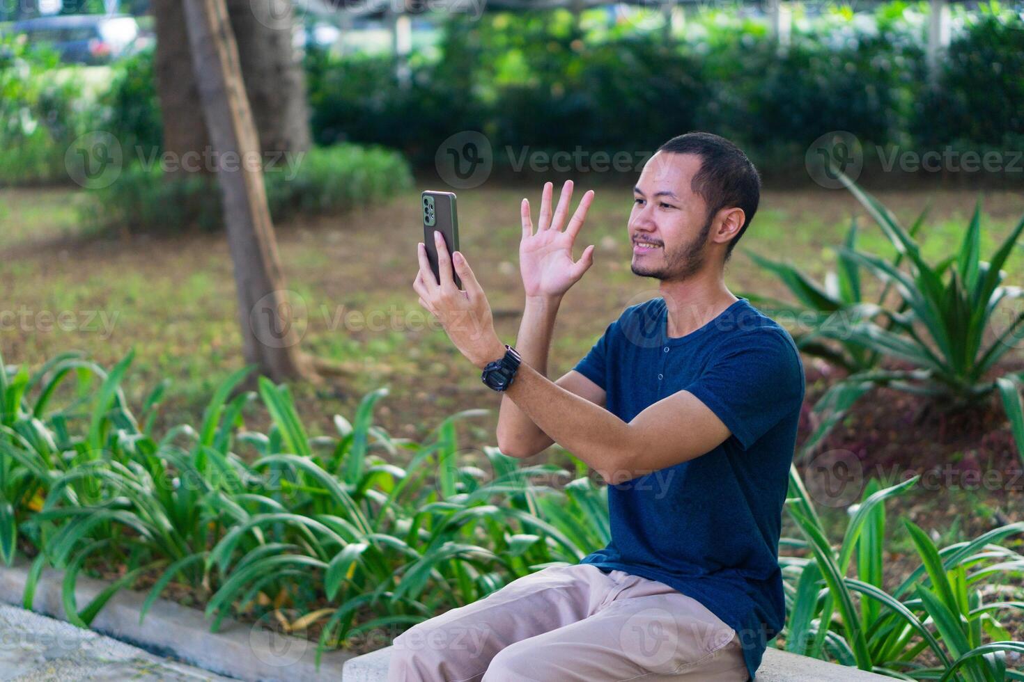 Young asian men with blue shirt smiling and laughing while playing smartphone on the park outdoor photo