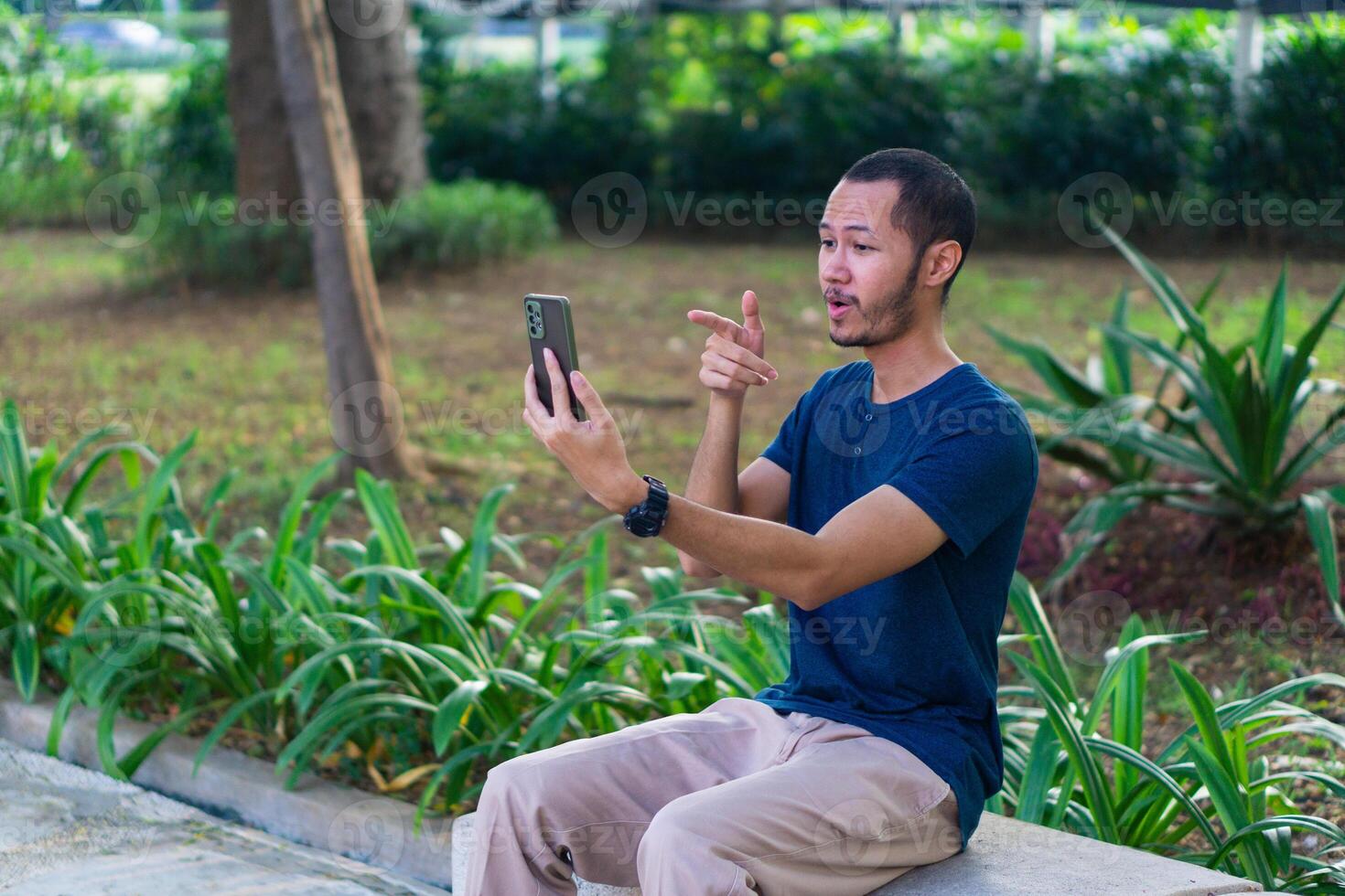 Young asian men with blue shirt smiling and laughing while playing smartphone on the park outdoor photo
